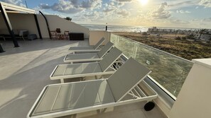 Eine Dachterrasse mit Liegestühlen, einem Tisch und Blick auf den Ozean.