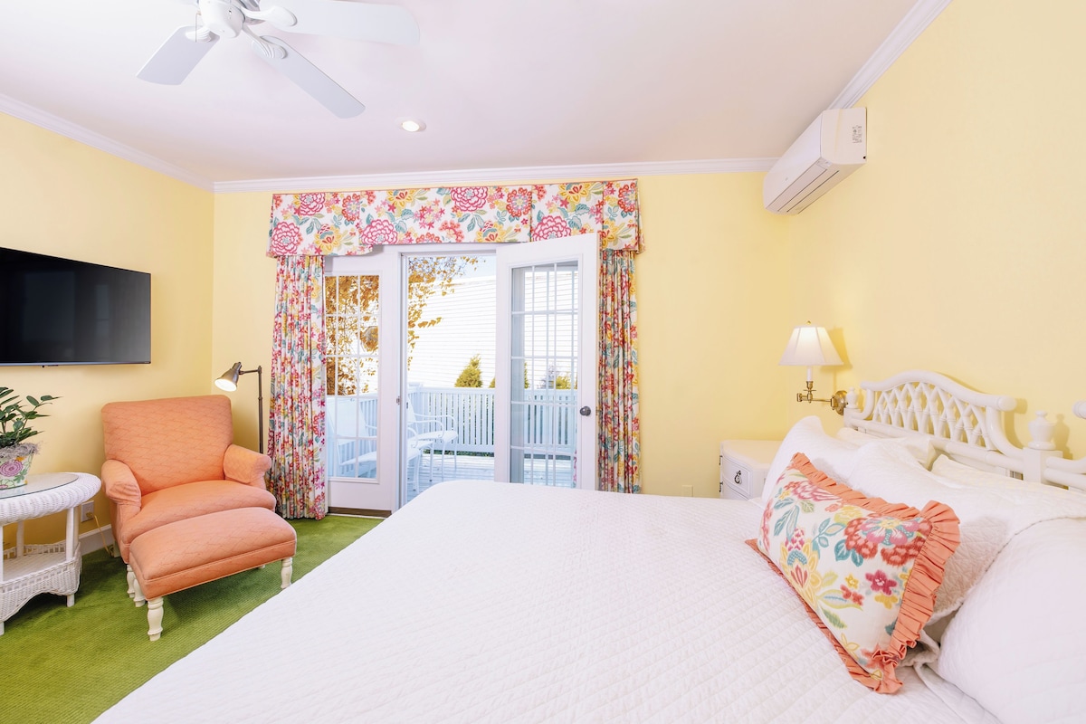 Un dormitorio con cama, una silla, una mesita, una lámpara y un ventilador de techo.