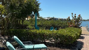 Ein gepflasterter Bereich mit zwei Liegestühlen, einer Holzterrasse und Blick auf das Wasser.