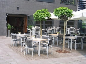 An outdoor patio with tables and chairs, trees, and a building in the background. - Contemporary Hotel with Easy Access to Breda and Rotterdam! Indoor Pool (Etten-Leur)