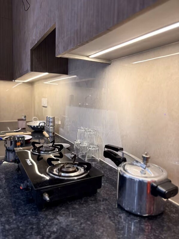 A kitchen with a gas stove, a kettle, and several glasses on the counter.