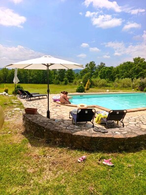 A pool area with lounge chairs, a stone wall, and a large umbrella. - ✨ Casale Caserinzio - Camellia (avigliano umbro)