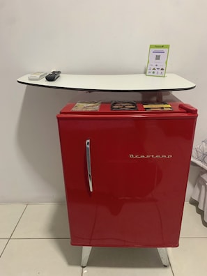 Un mobiletto rosso con una maniglia, un tavolo bianco con un codice QR e un telecomando sul mobiletto.