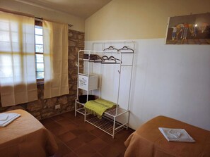 A room with two beds, a metal drying rack, a stone wall, and a painting on the wall. - Casale Caserinzio | Nature, History and Relaxation in the Heart of Umbria (Avigliano Umbro, Terni)
