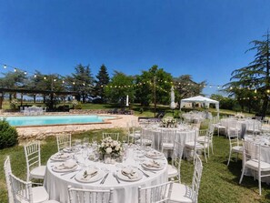 Eine Hochzeitsfeier im Freien mit runden Tischen, weißen Stühlen und einem Pool.