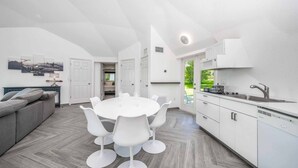 A modern kitchen with white cabinets, a dining area with a white table and chairs, and a grey sofa.
