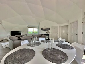 Een eetgedeelte met een ronde tafel, witte stoelen en geweven placematen.