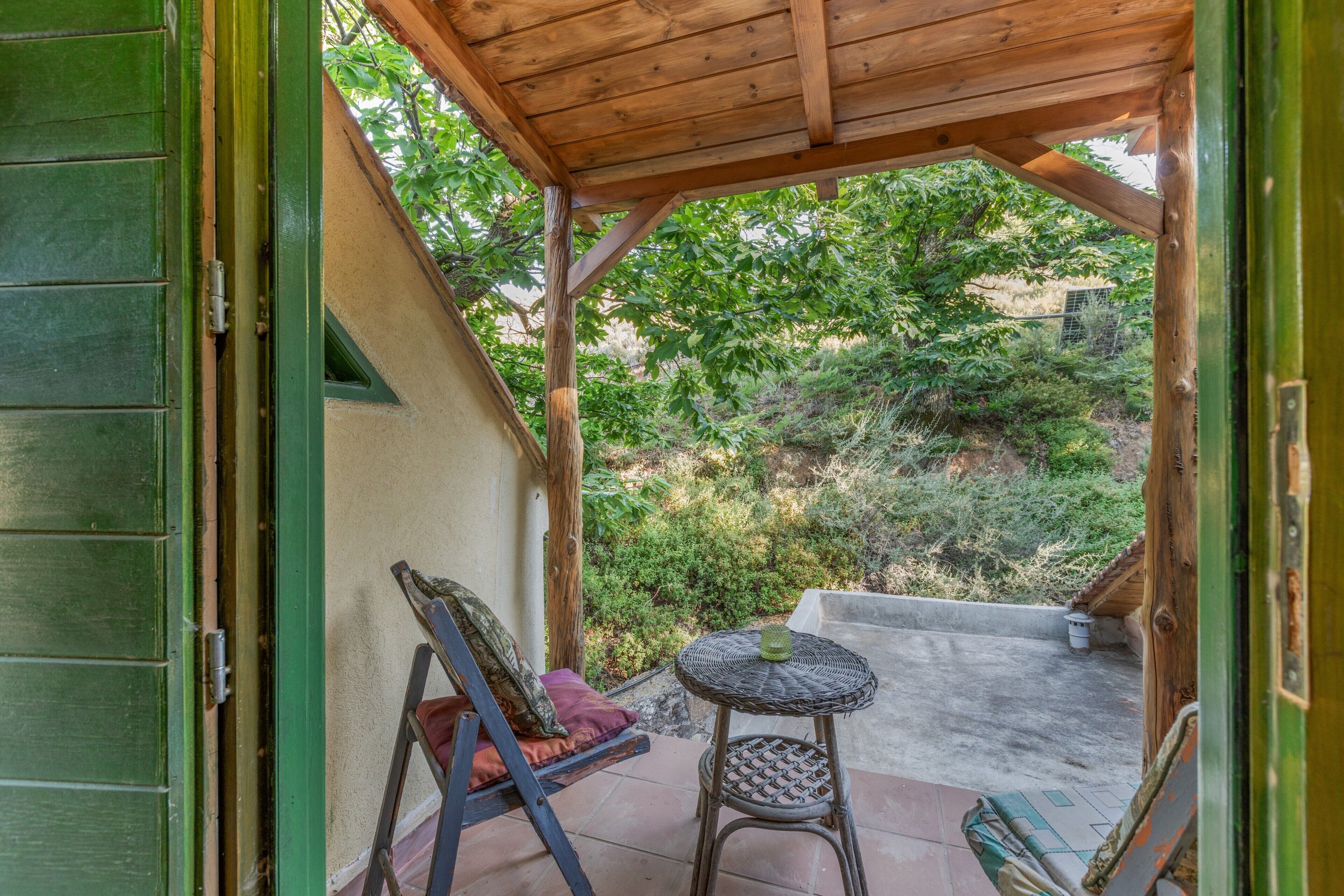 An open wooden door leading to a covered patio with a wicker table and a cushioned chair.