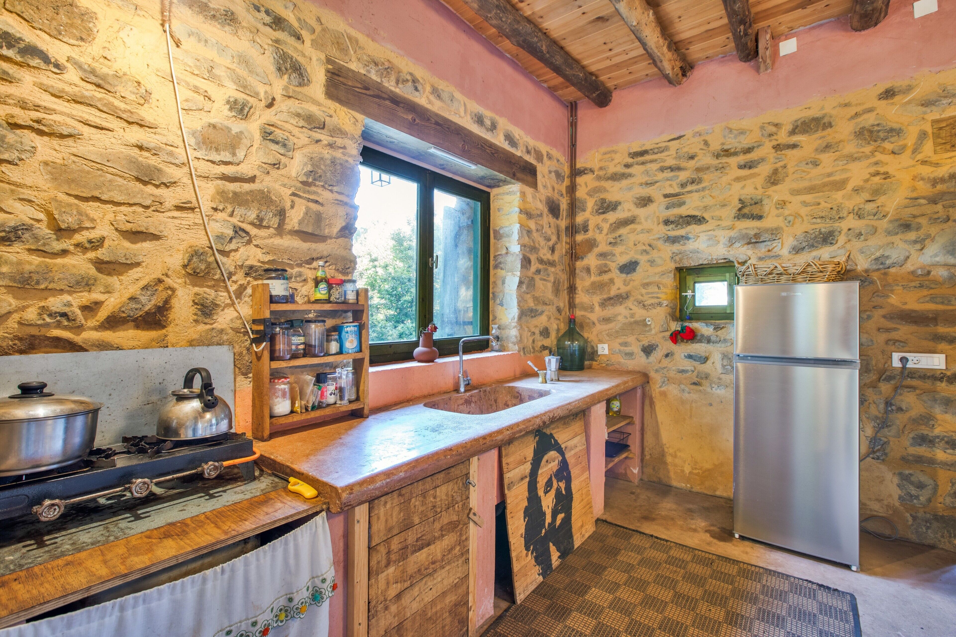 A rustic kitchen with stone walls, a wooden counter, a stove, a sink, and a refrigerator.