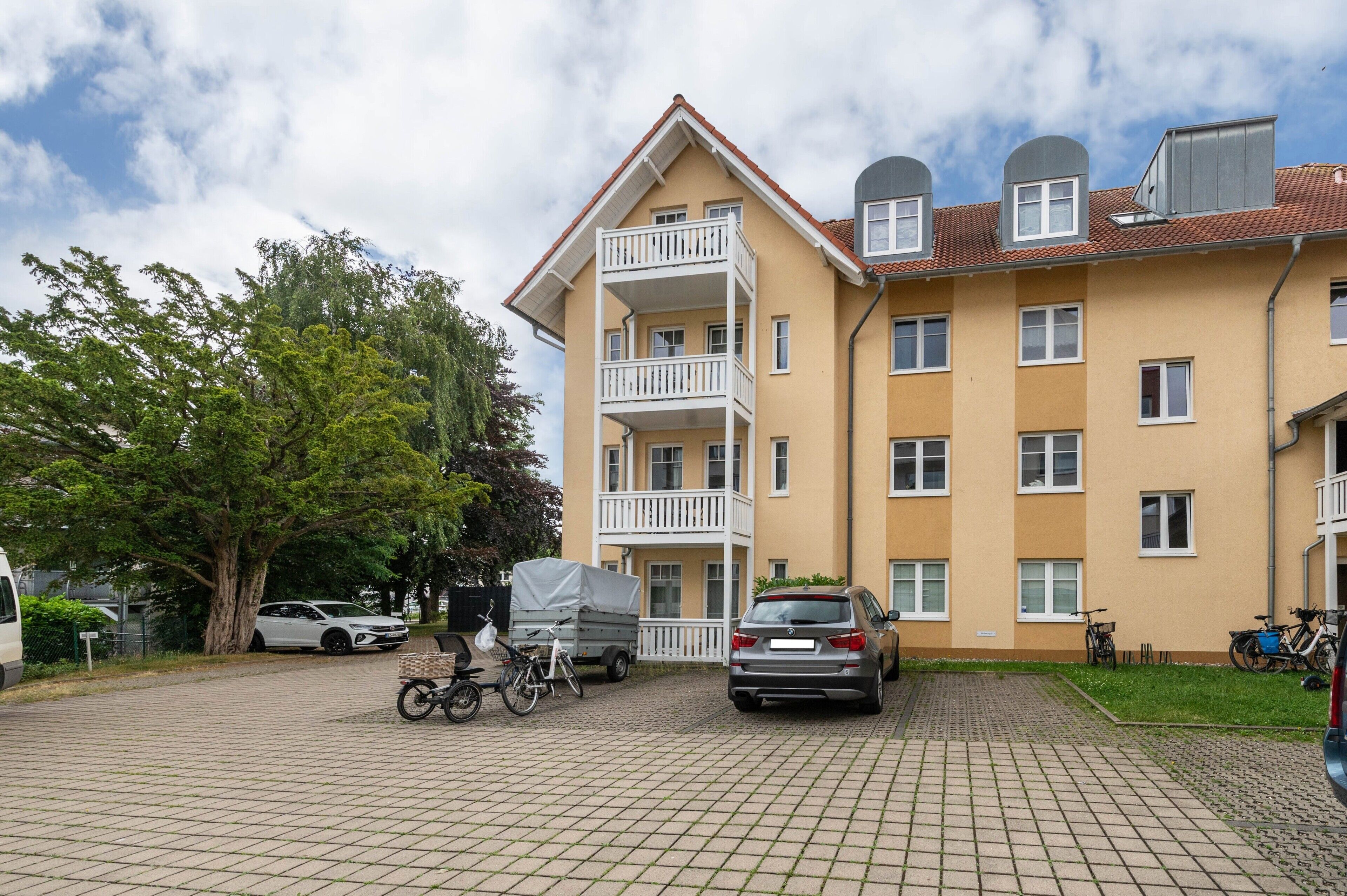 En flervåningsbostadsbyggnad med balkonger, ett takbeklädd carport och en asfalterad uppfart.