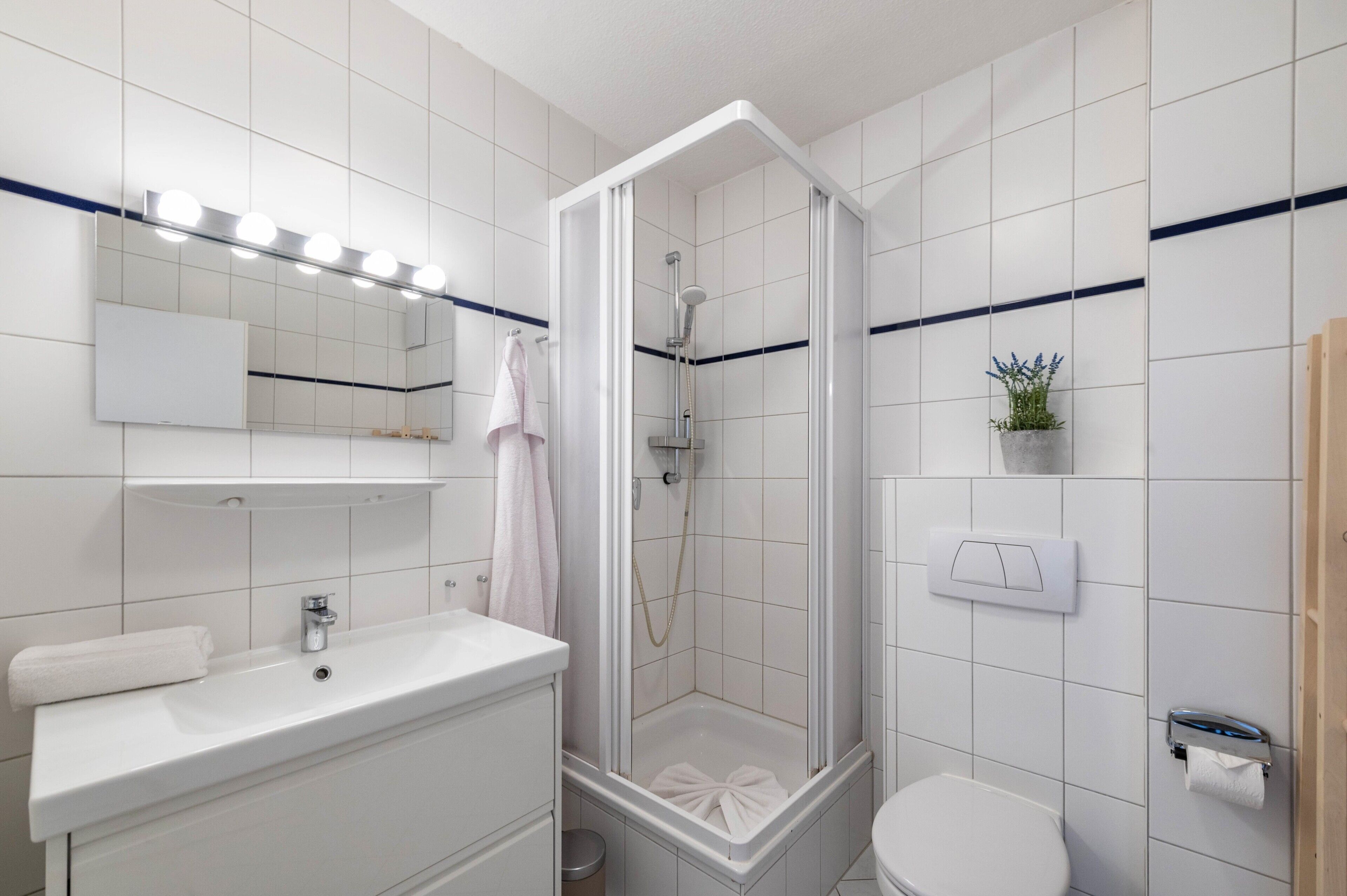 Un baño moderno con ducha, lavabo, inodoro y un espejo con luces.