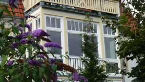 Ein Gebäude mit vielen Fenstern, einem Balkon und umgebender Bepflanzung.