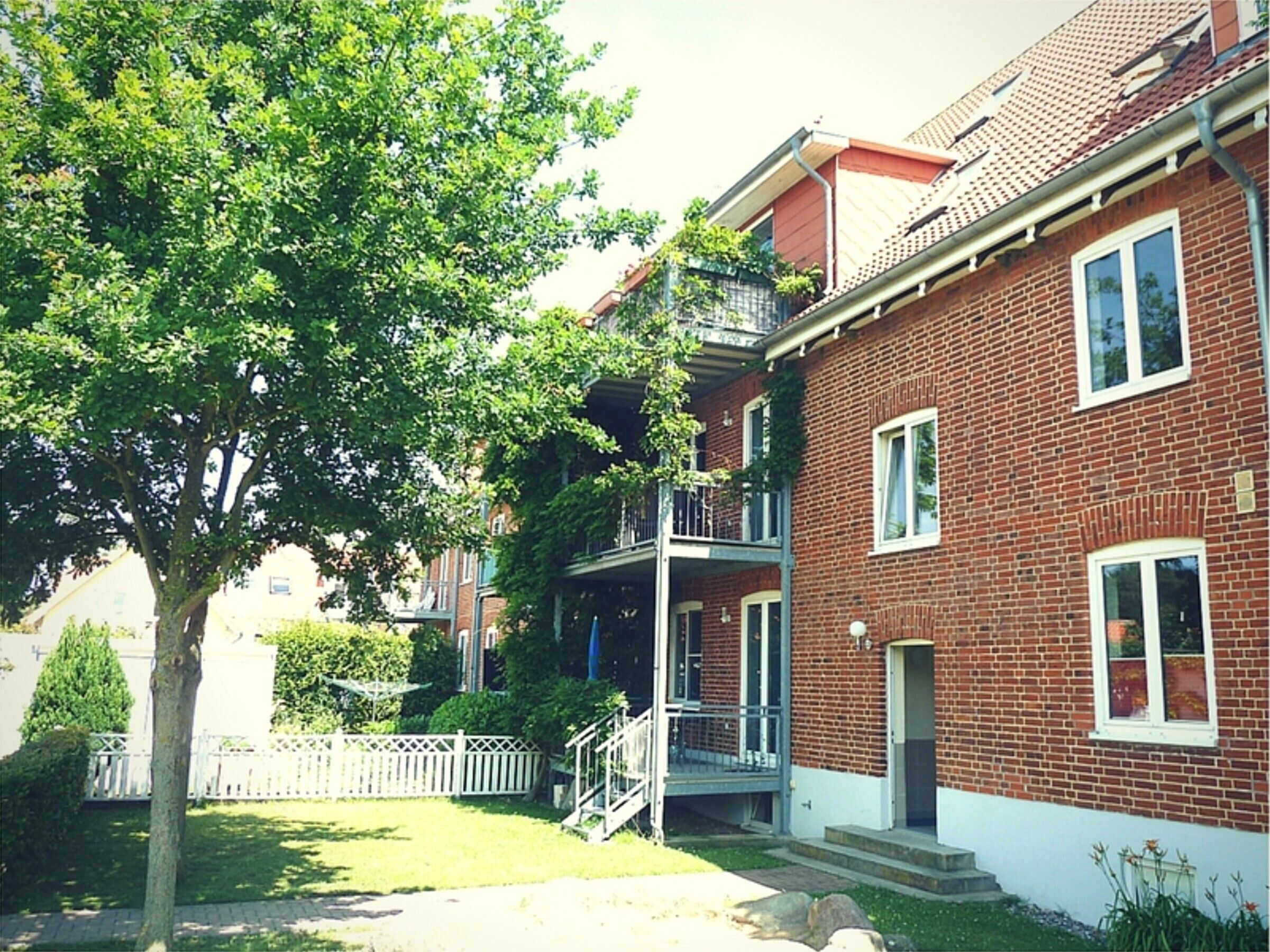 A two-story brick building with a white trim, a front porch, and a tree in the yard.