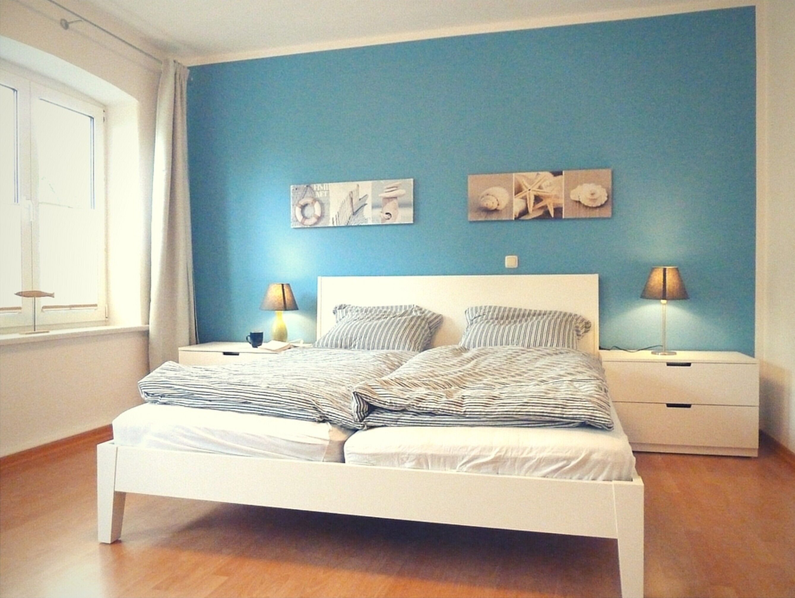 Ein Schlafzimmer mit einem Doppelbett, zwei Nachttischen, einem Fenster und Wandbildern.
