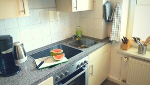 Une cuisine équipée d’une cuisinière, d’un évier et d’un plan de travail sur lequel se trouvent une planche à découper et une pastèque.