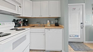 Een keuken met witte kastjes, een fornuis, een vaatwasser, een spoelbak en een blender.