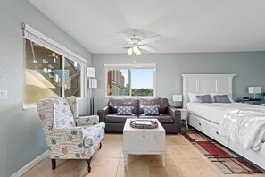 Ein Zimmer mit Sofa, Sessel, Bett, Deckenventilator und Fenster.