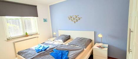 A bedroom with a bed, bedside tables, a wall clock, and a window with blinds.