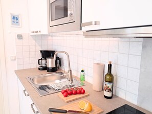 Eine Küche mit Spüle, Kaffeemaschine, einer Weinflasche und einem Schneidebrett mit Tomaten und Zitrone.
