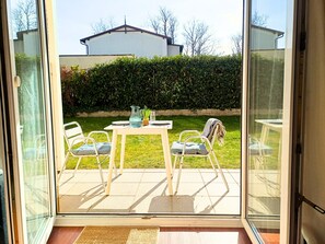Eine Terrasse mit Tisch und Stühlen, eine Glastür und im Hintergrund ein Hecke und ein Haus.