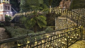 Un escalier en pierre avec des rampes en métal, entouré de verdure et bordé d’un bâtiment aux fenêtres en arc de cercle.
