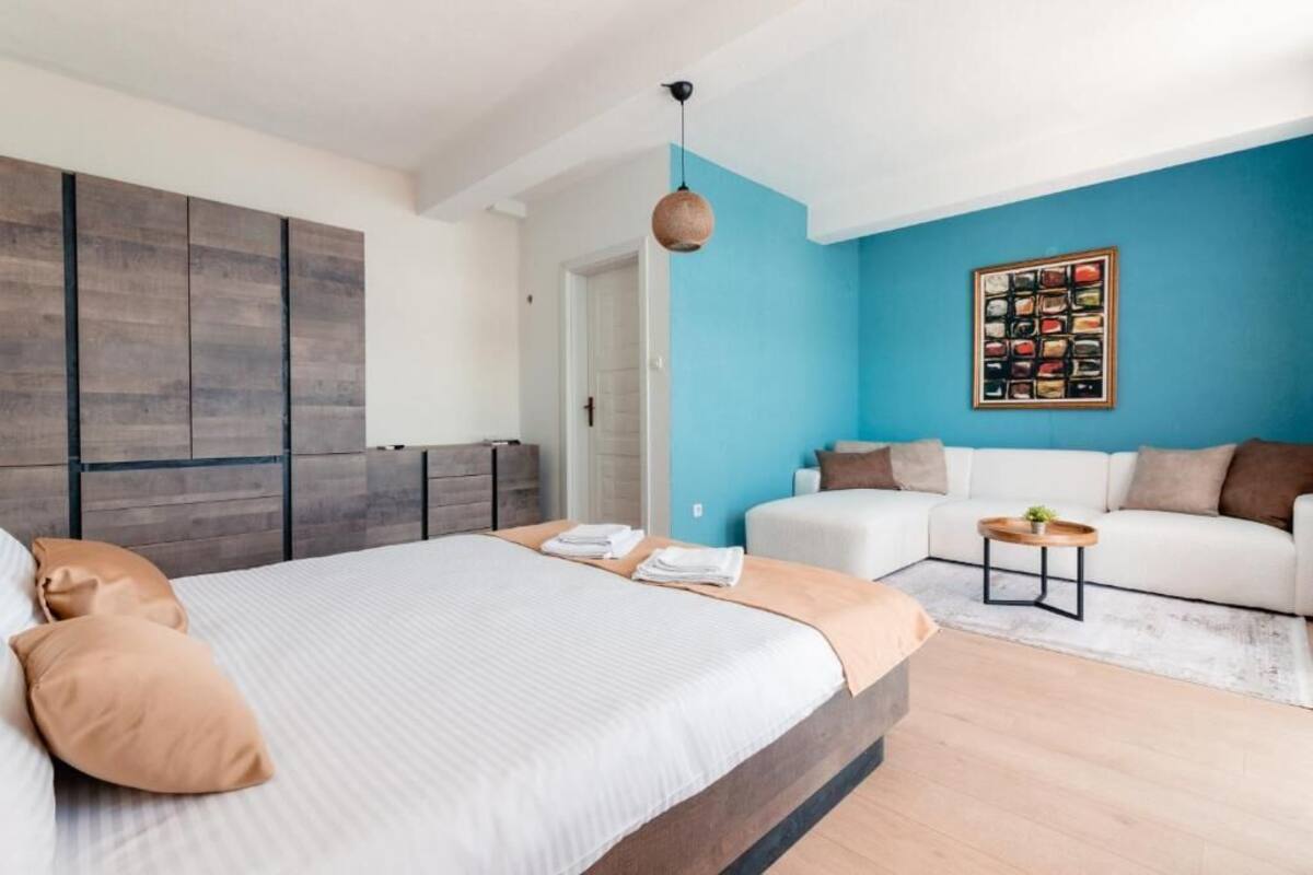 Un dormitorio moderno con una cama grande, un sofá blanco, una pared de acento azul y un cuadro enmarcado.