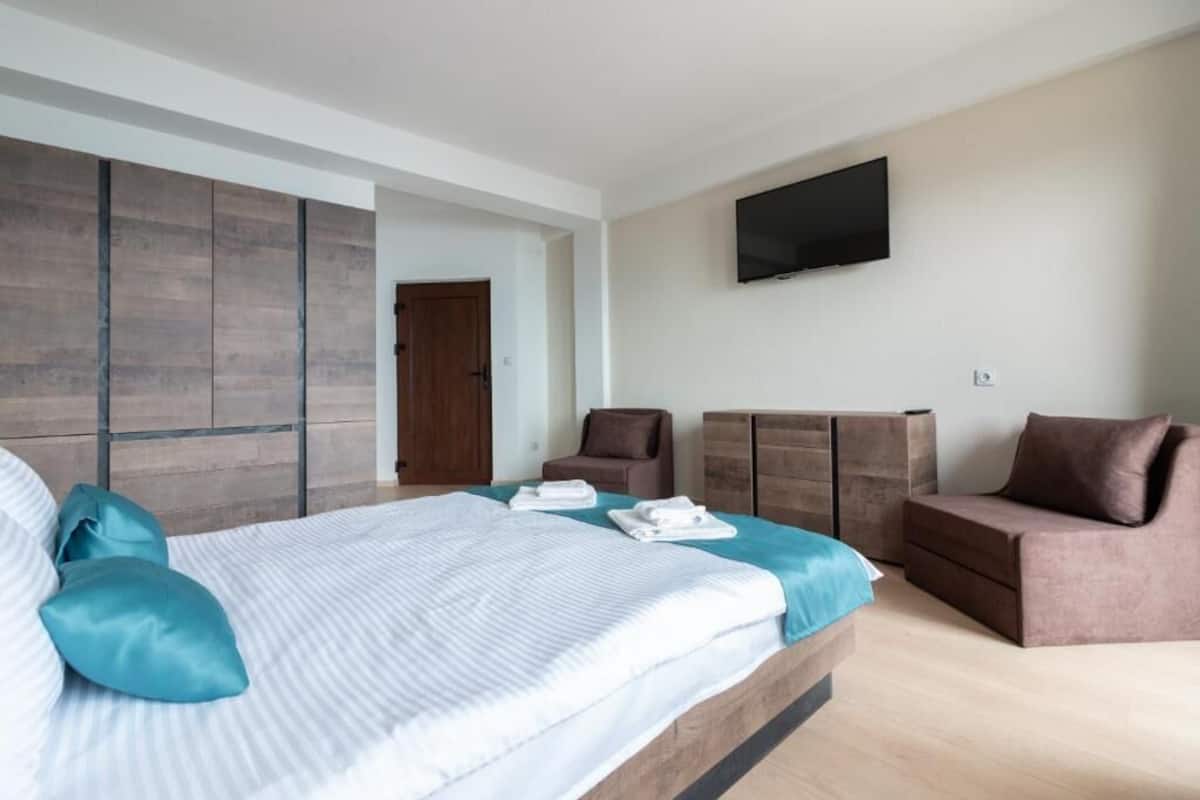 Una habitación de hotel moderna con una cama grande, un televisor de pantalla plana, un armario de madera y una zona de estar.