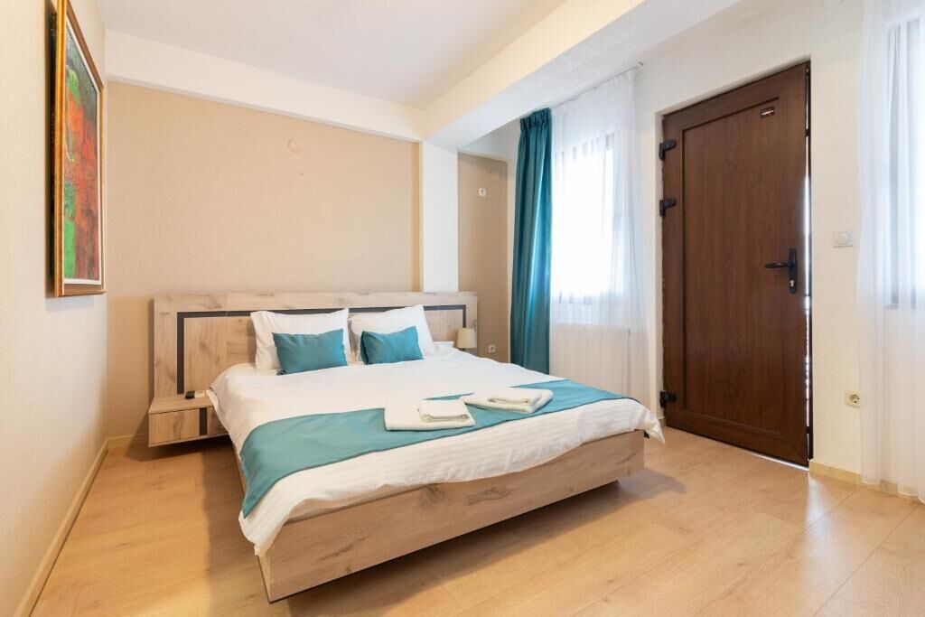 A bedroom with a bed, a nightstand, a wooden headboard, a door, and a window with curtains.