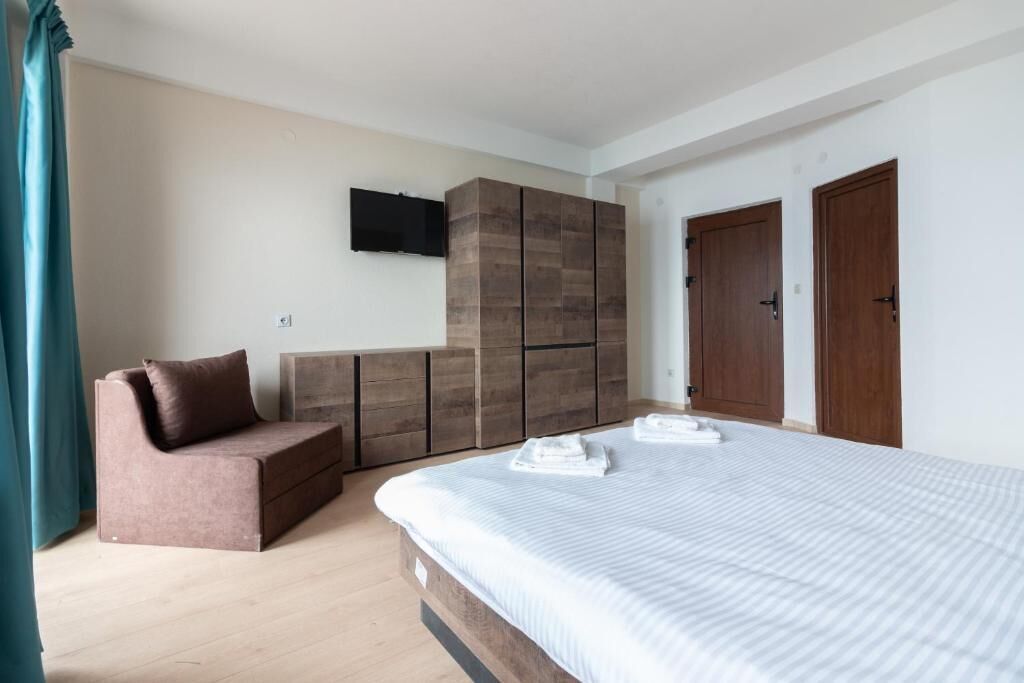 A bedroom with a bed, a sofa, a wardrobe, and a TV mounted on the wall.