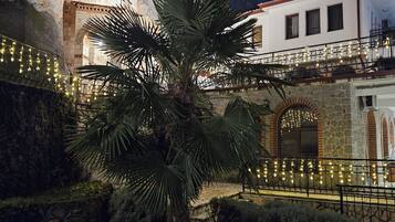 Un bâtiment à la façade en pierre, avec un palmier et un balcon décoré de guirlandes lumineuses.