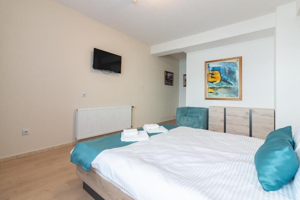 A bedroom with a bed, a television, a painting, and a radiator.