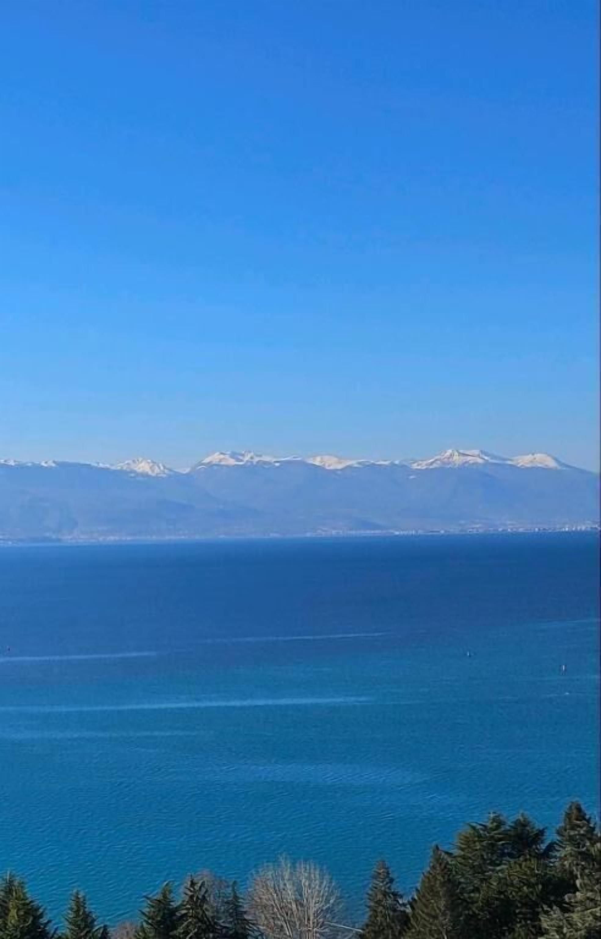Un paysage côtier avec un ciel dégagé, une étendue d’eau et, au loin, des montagnes aux sommets enneigés.