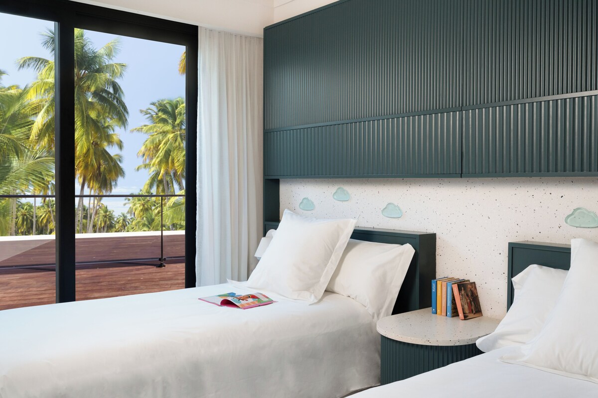 A hotel room with a large window, a bed, a bedside table, and a view of palm trees.