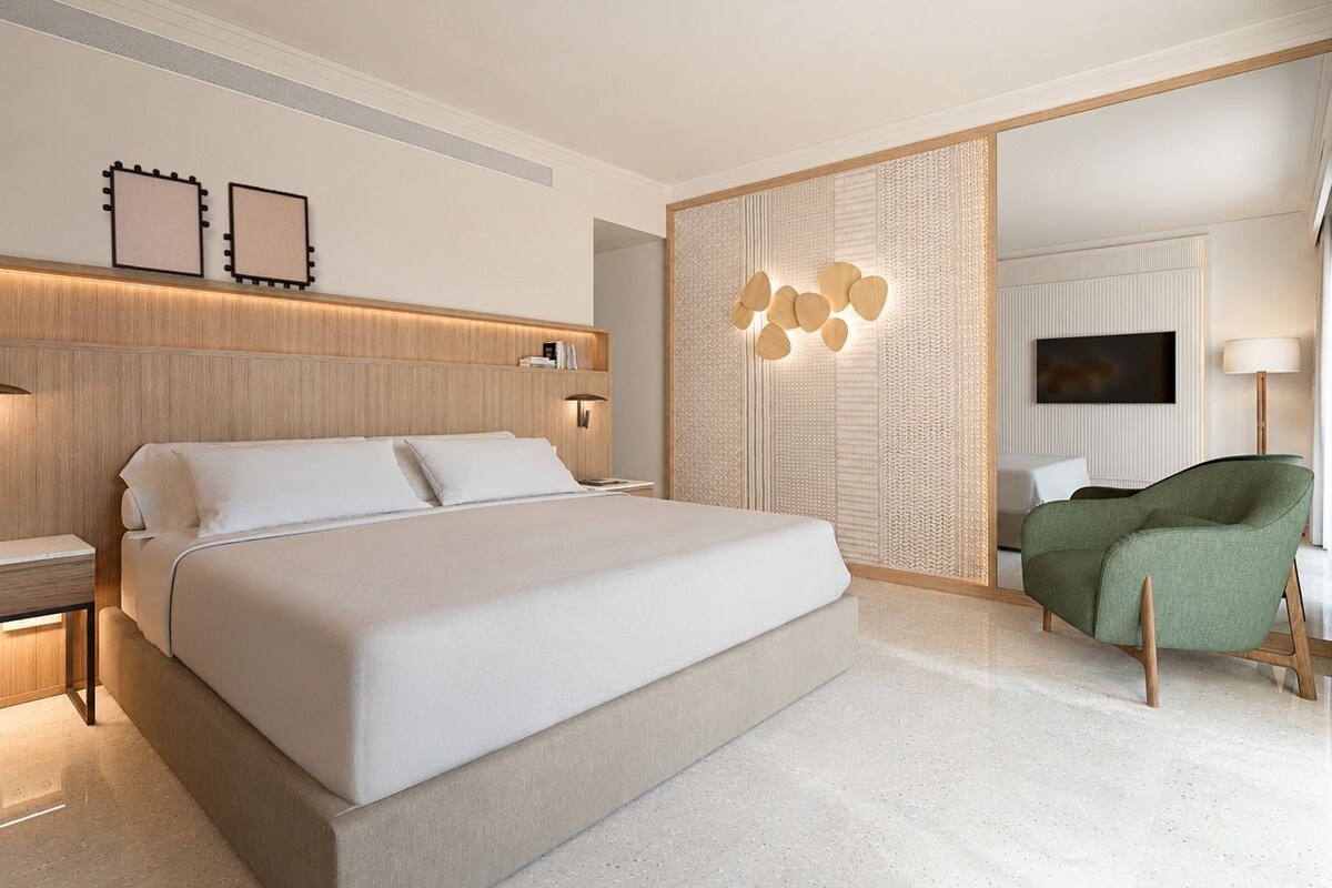 A modern hotel room with a large bed, a green armchair, and a TV on the wall.