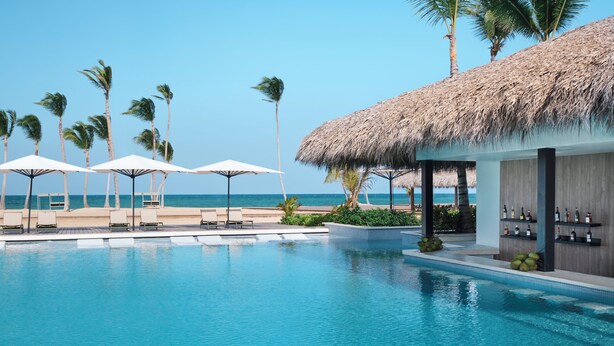 Un espace piscine avec des chaises longues et des parasols, un bar avec des bouteilles et des palmiers.