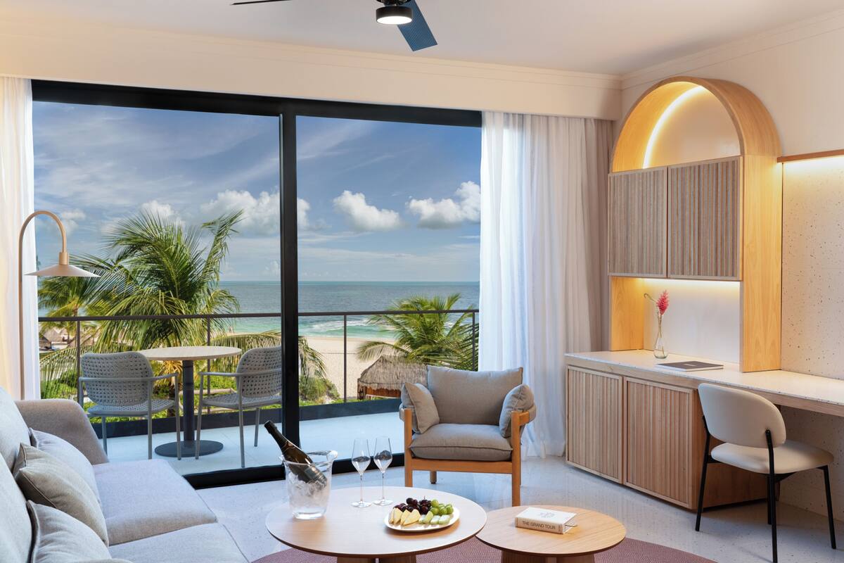 Una habitación de hotel moderna con balcón, sofá, mesa de comedor y escritorio.