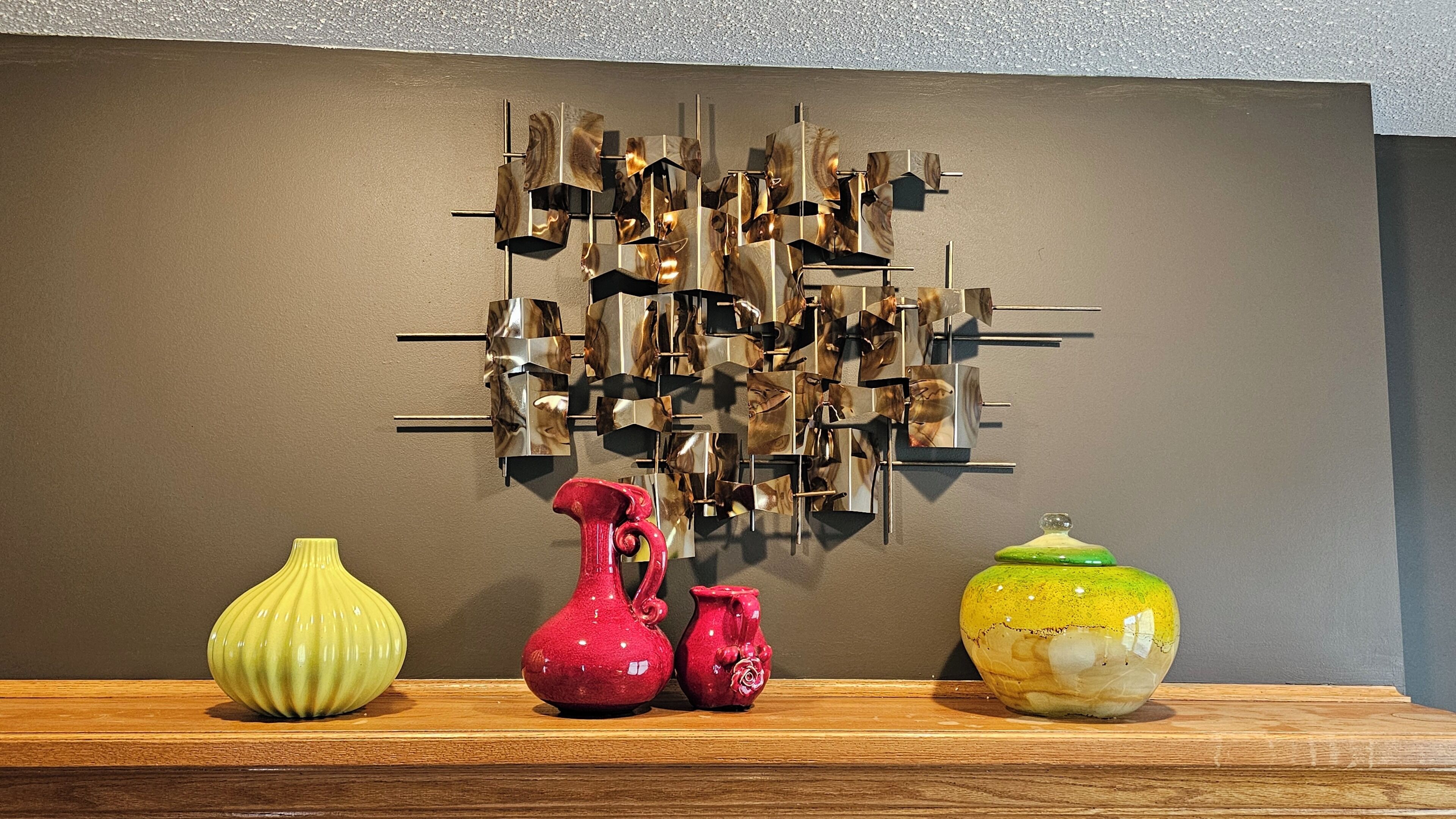 Un mur orné d’une œuvre d’art géométrique et sur lequel sont posés trois vases en céramique, le tout sur une étagère en bois.