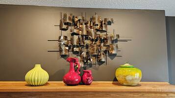 Un mur orné d’une œuvre d’art géométrique et sur lequel sont posés trois vases en céramique, le tout sur une étagère en bois.