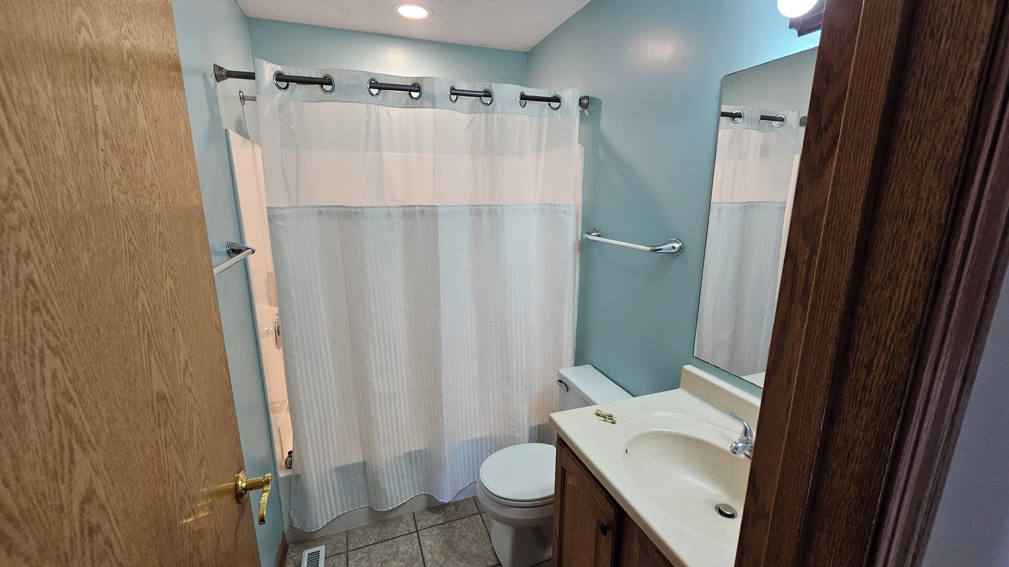 Une salle de bain équipée d’un rideau de douche, de toilettes, d’un lavabo et d’un miroir.