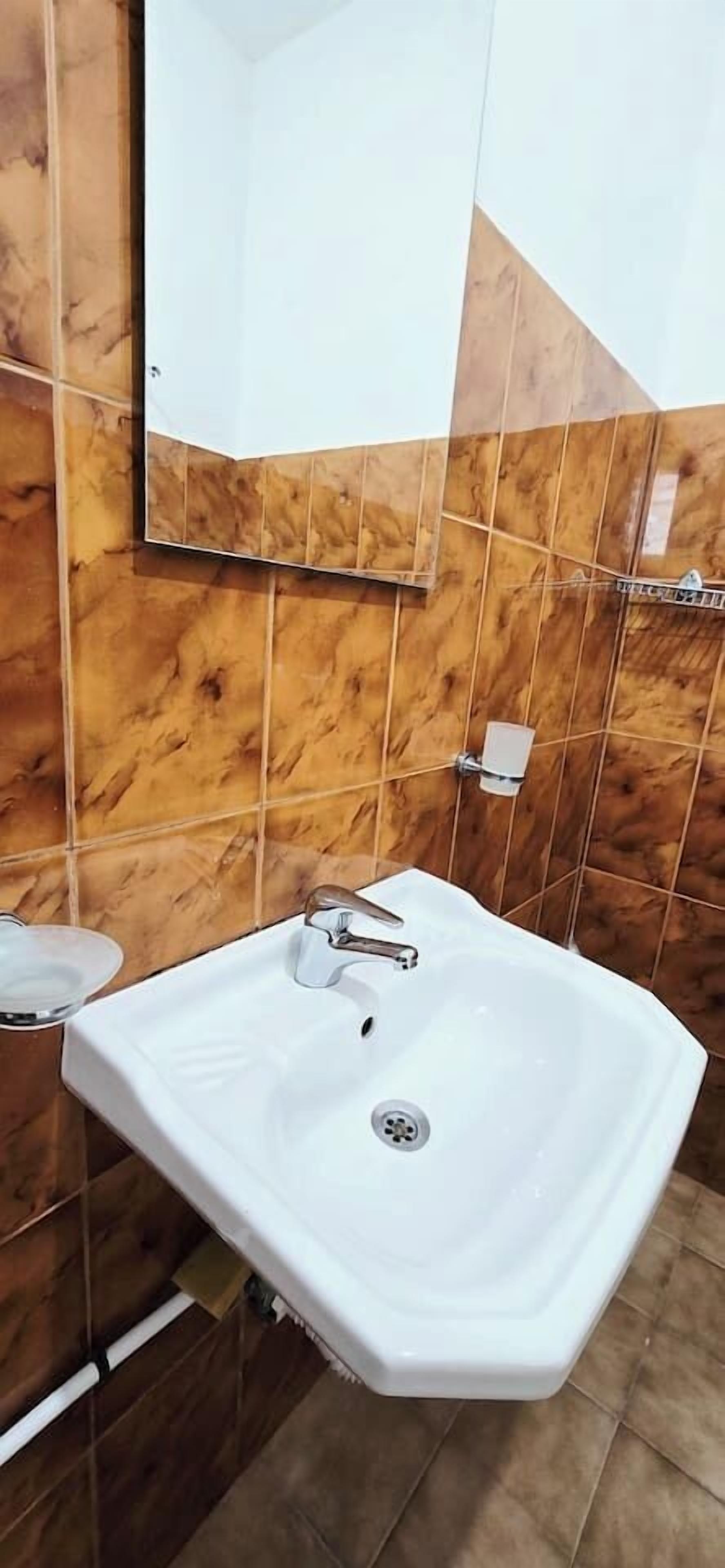 Een badkamer met een wit wastafelmeubel, een spiegel en bruine marmeren tegels.