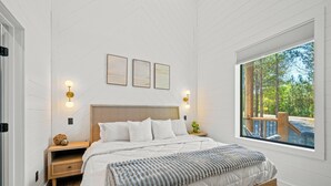 Ein Schlafzimmer mit einem großen Bett, zwei Wandleuchten und einem Fenster mit Blick auf Bäume.