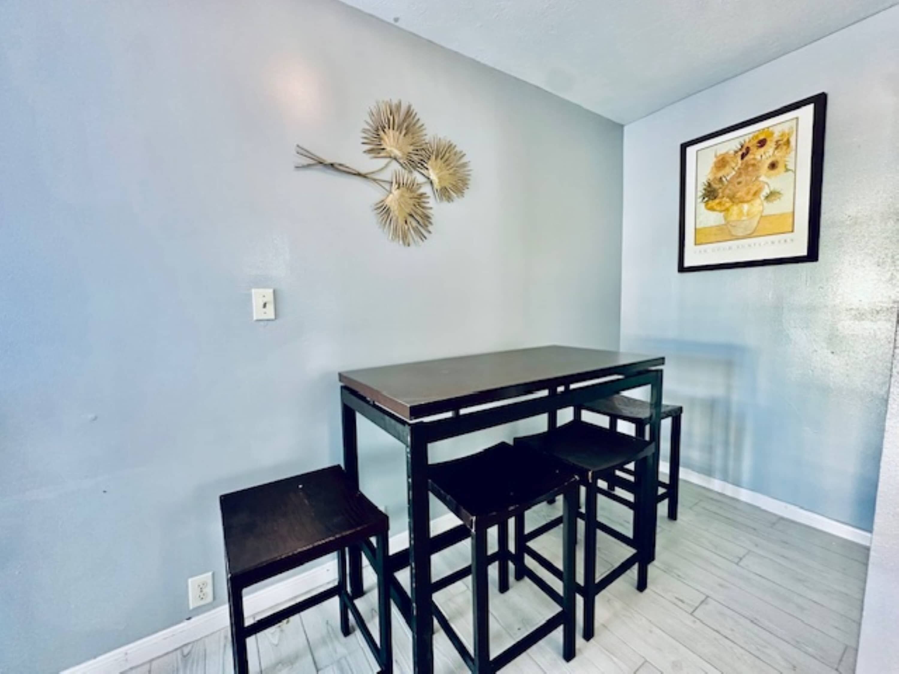 A dining area with a table and four chairs, a wall-mounted decorative piece, and a framed picture.