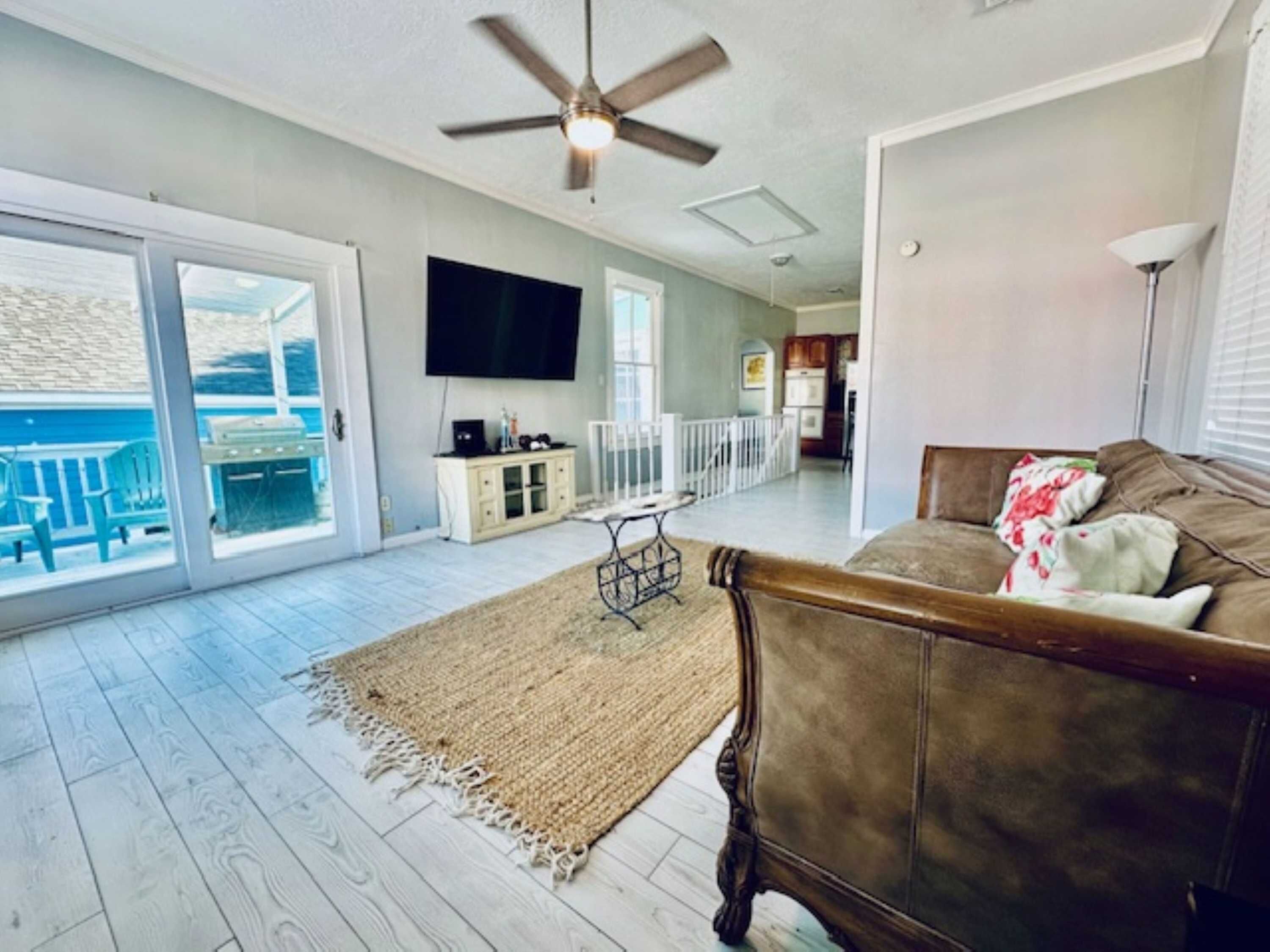 A living room with a ceiling fan, a TV, a sofa, and a view to the outside.