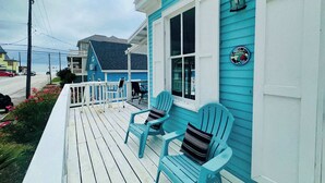 Une maison bleue avec un porche, deux chaises et un petit panneau.