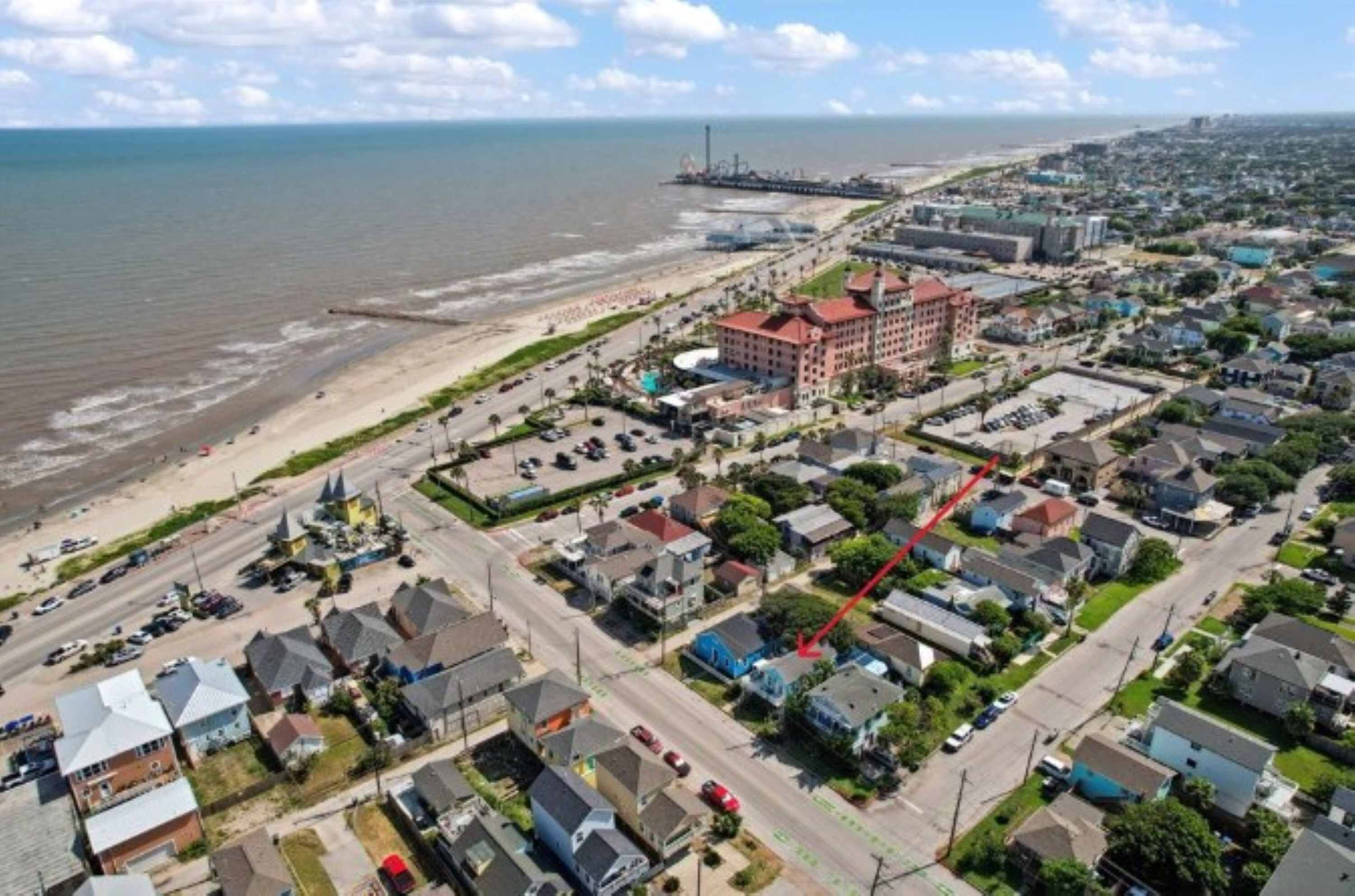 An aerial view of a coastal town with a prominent hotel, a beach, and a pier in the background.