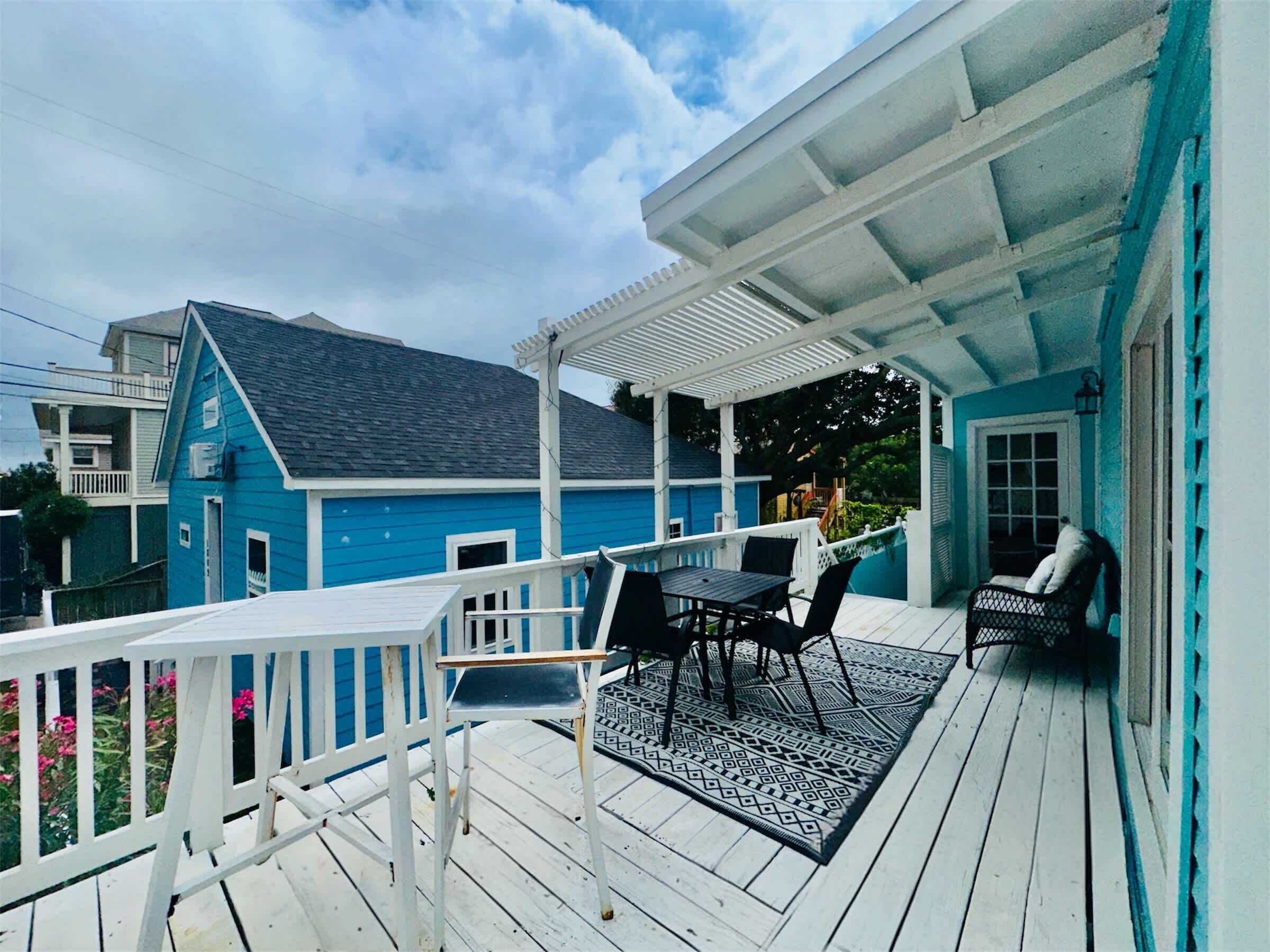 A blue house with a porch, a table with chairs, and a covered area.
