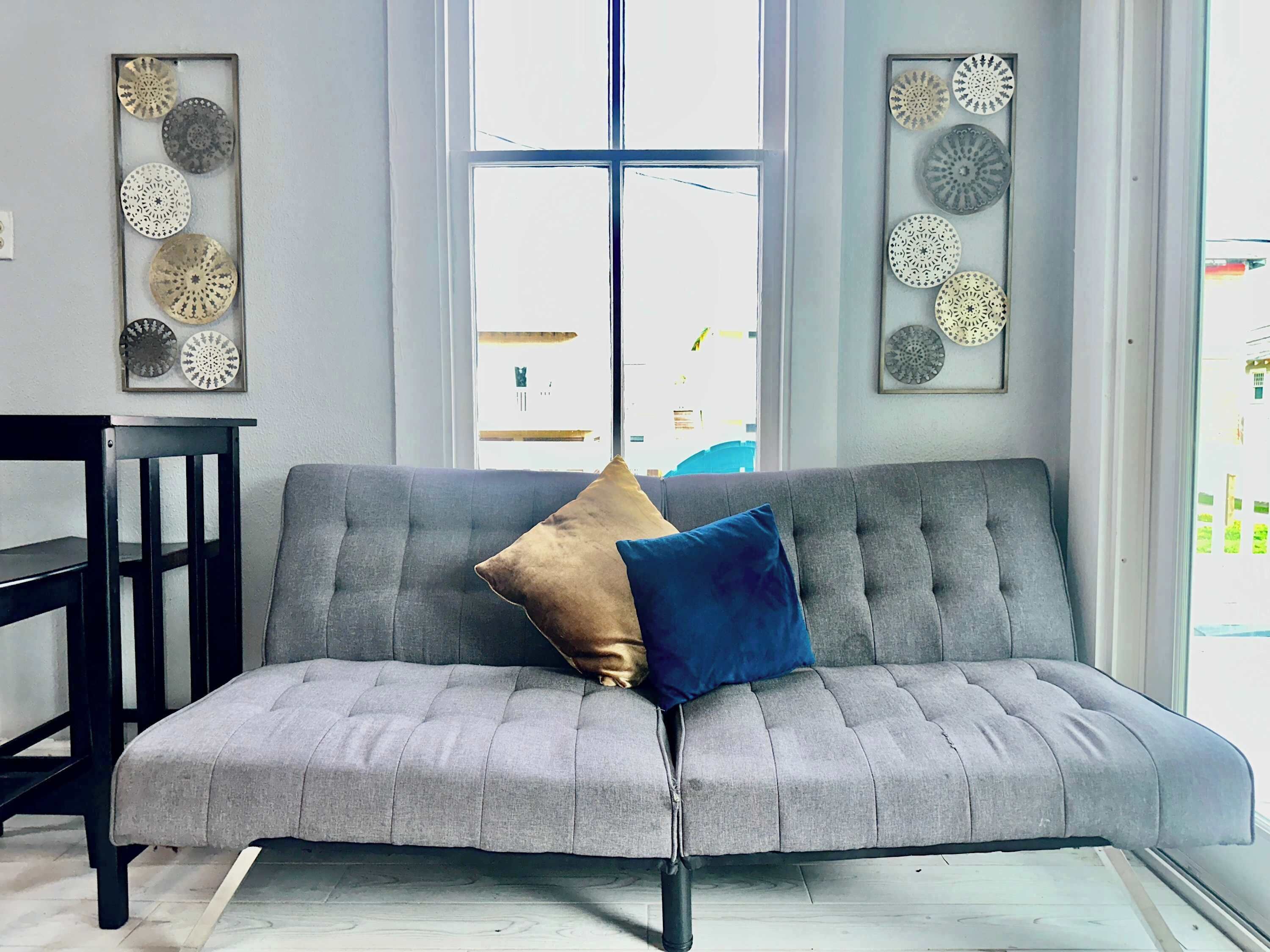 A grey sofa with a blue and beige cushion, a black chair, and decorative plates on the walls.
