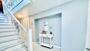 Un escalier avec des rampes blanches et un plancher en bois, menant à un palier où se trouve une console blanche et un petit objet décoratif.