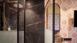 A bathroom with a marble wall, a gold shower, a sink with a marble basin, a towel, and a mirror. - The Place Brussels (Brussels)