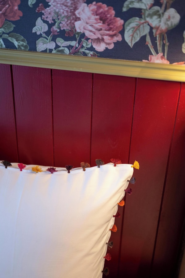 Una habitación con cabecera de madera roja, almohada blanca con flecos y un estampado floral en el papel tapiz.